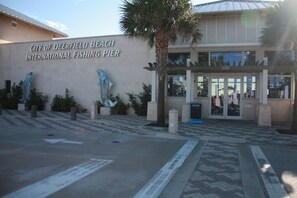 The entrance to the City of Deerfield Beach International Fishing Pier with a clear sign, a palm tree, and a building entrance. - Beachside Villa - Ocean 100 Ft. (Deerfield Beach)