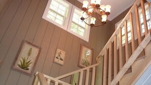 Un escalier en bois surmonté d’un lustre, des reproductions botaniques encadrées accrochées au mur et de grandes fenêtres laissant entrer la lumière naturelle.