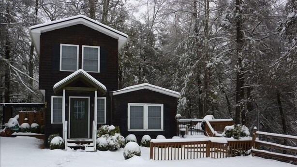 Une cabane à deux étages, dotée d’un porche à l’avant et d’une terrasse, entourée d’arbres couverts de neige.