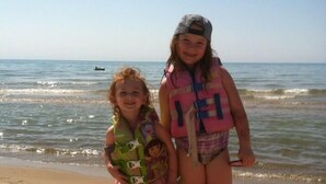 Deux enfants sur une plage de sable, avec l’océan en arrière-plan.