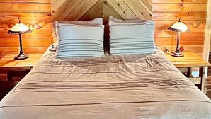 Un lit recouvert d’une couvre-lit à rayures, dans une pièce aux murs en bois et dotée de deux lampes de chevet.