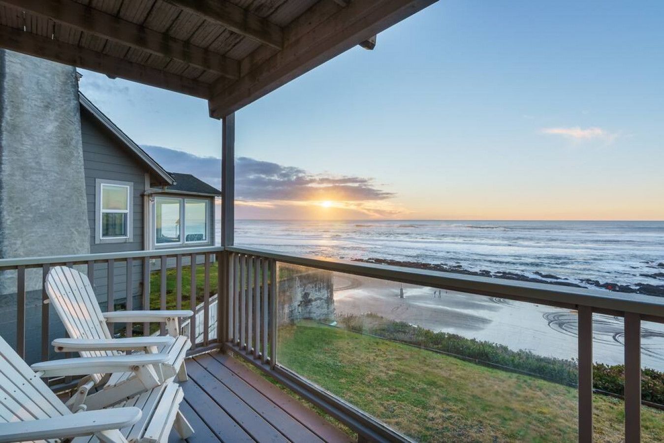 Een houten terras met Adirondack-stoelen, uitkijkend op een strand bij zonsondergang.