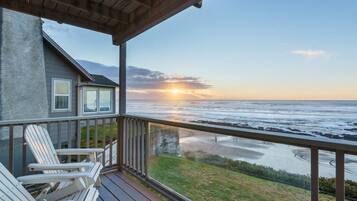 Een houten terras met Adirondack-stoelen, uitkijkend op een strand bij zonsondergang.