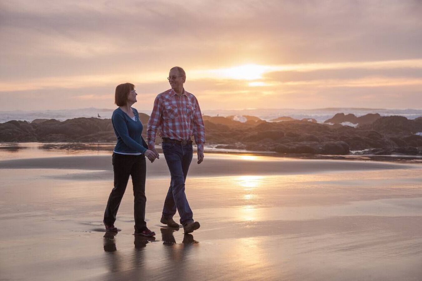 Una pareja caminando por una playa con el atardecer al fondo.