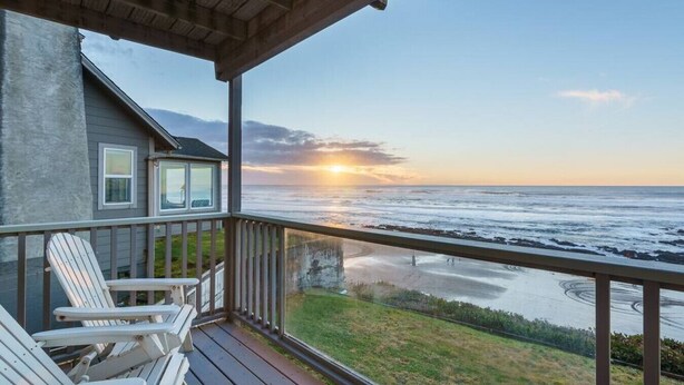 Eine Holzterrasse mit Adirondack-Stühlen mit Blick auf einen Strand bei Sonnenuntergang.