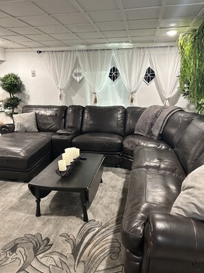 A modern living room with a dark leather sectional sofa, a black coffee table, and a grey patterned rug.