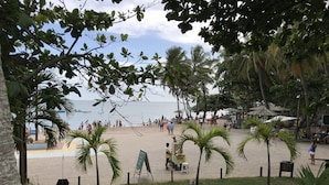 A beach with palm trees, a volleyball net, and people in the distance. - Apartamento Porto Praia do Forte (Mata de São João)