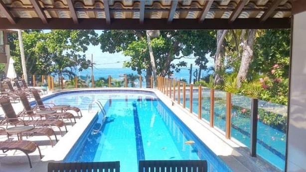 A swimming pool with lounge chairs and a view of the ocean. - Apartamento Porto Praia do Forte (Mata de São João)