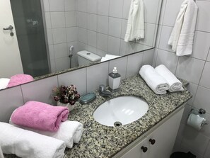 A bathroom with a granite countertop, white sink, and a mirror. There are towels, a soap dispenser, and a toilet paper holder visible.