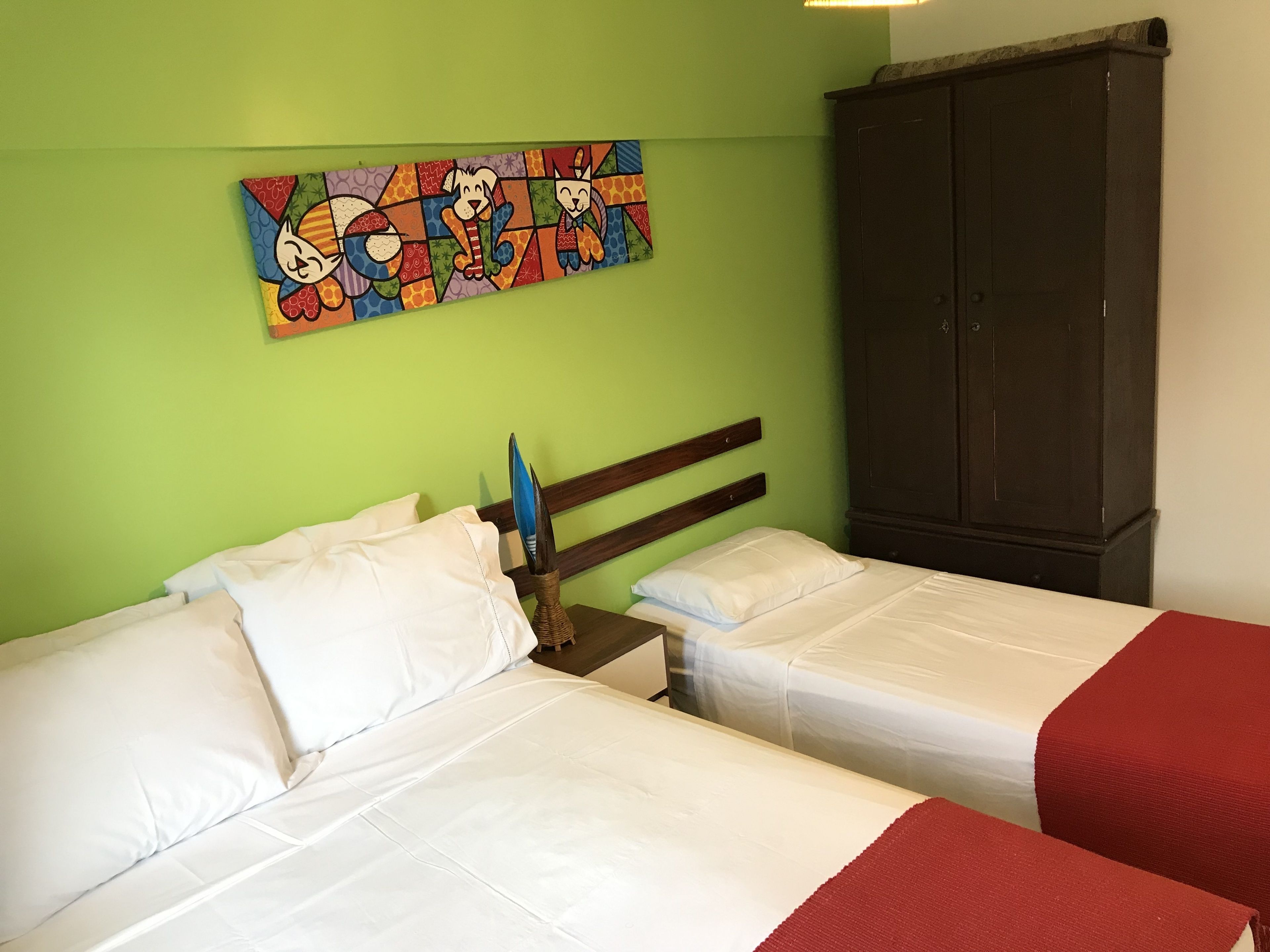 Quarto com duas camas, cabeceira de madeira, guarda-roupa escuro e um quadro colorido na parede.