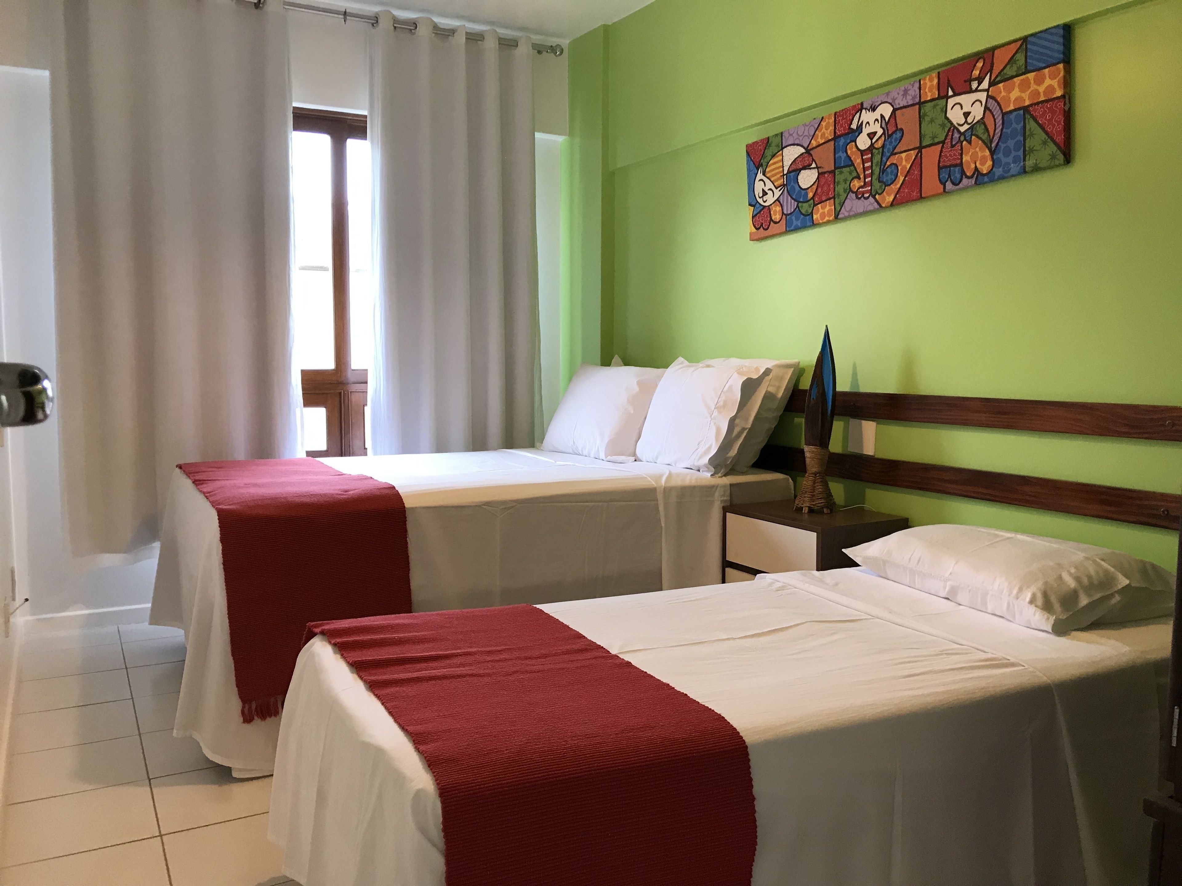 Quarto de hotel com duas camas, uma parede verde e um quadro colorido.