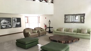 A spacious living room with a high ceiling, a large mirror, and two sofas. - Apartamento Porto Praia do Forte (Mata de São João)
