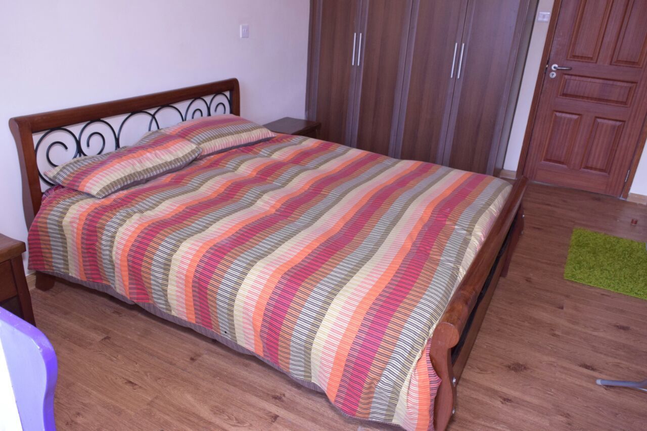 Une chambre à coucher avec un lit en bois, une literie à rayures, un tapis vert et une armoire en bois.