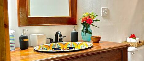 Un baño con tocador de madera, espejo, lavabo y cestas de mimbre debajo del mueble.