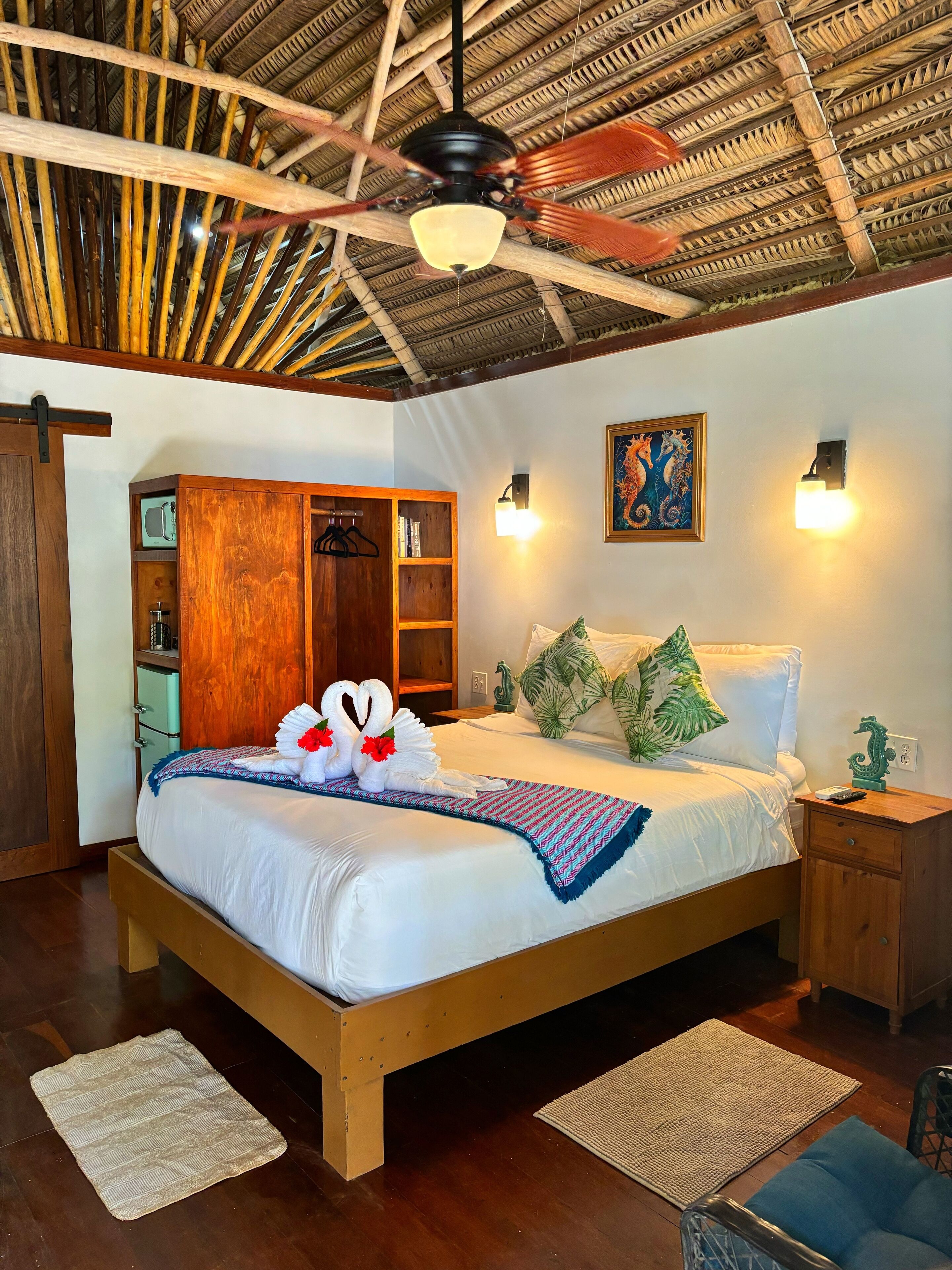 A well-lit bedroom with a wooden bed, a ceiling fan, a wardrobe, and a nightstand.