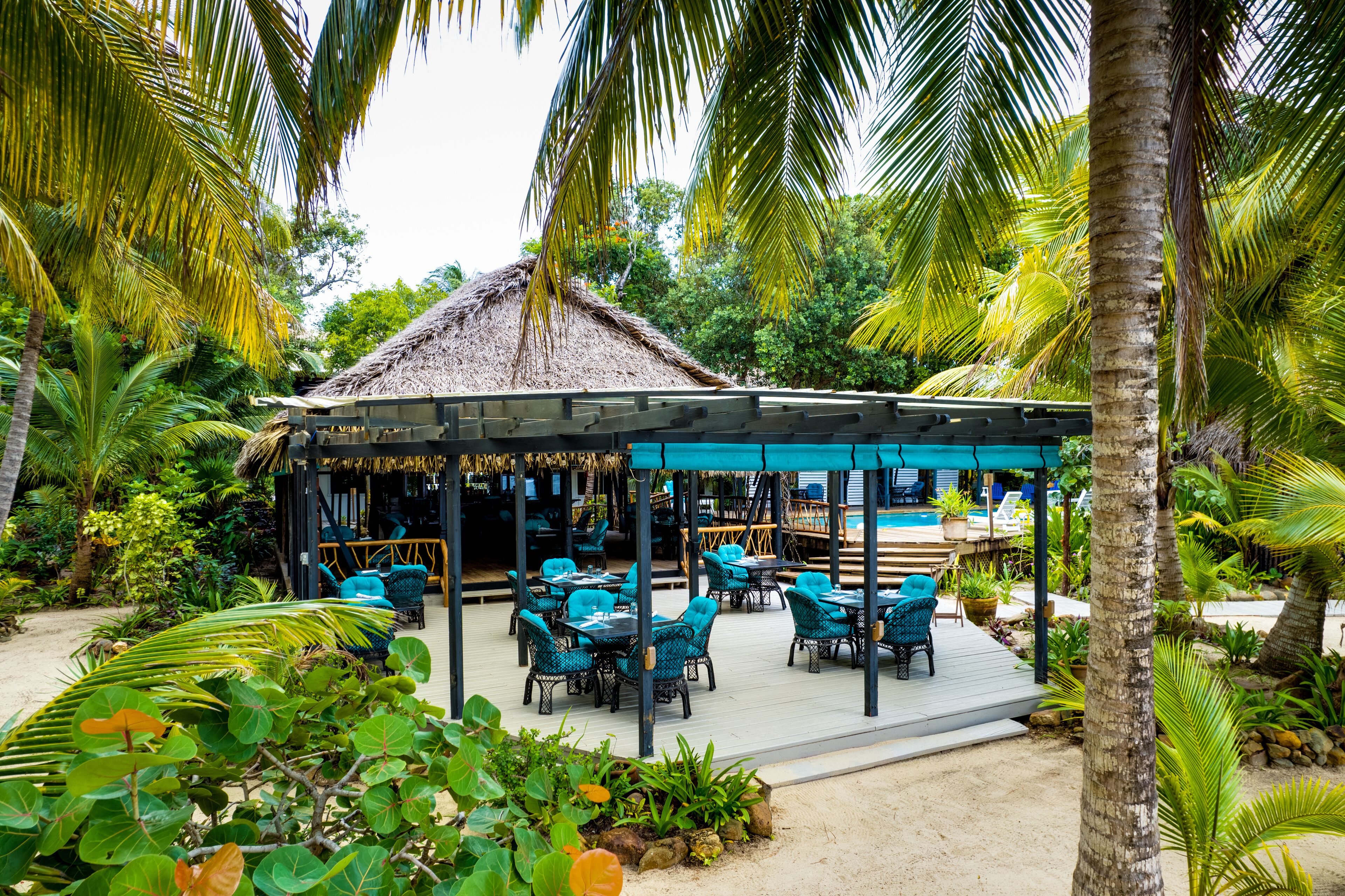 An outdoor seating area with thatched-roof tables and chairs, surrounded by lush tropical vegetation.