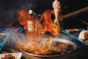 A grill with food being cooked over an open flame, a bottle of beer, and a plate of rice. - Azure Del Mar (Placencia)