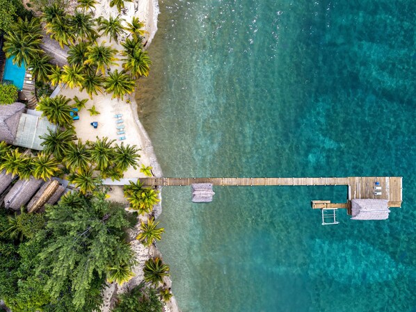 An aerial view of a beach with a wooden pier connecting to a bungalow with a balcony. - Azure Del Mar (Placencia)
