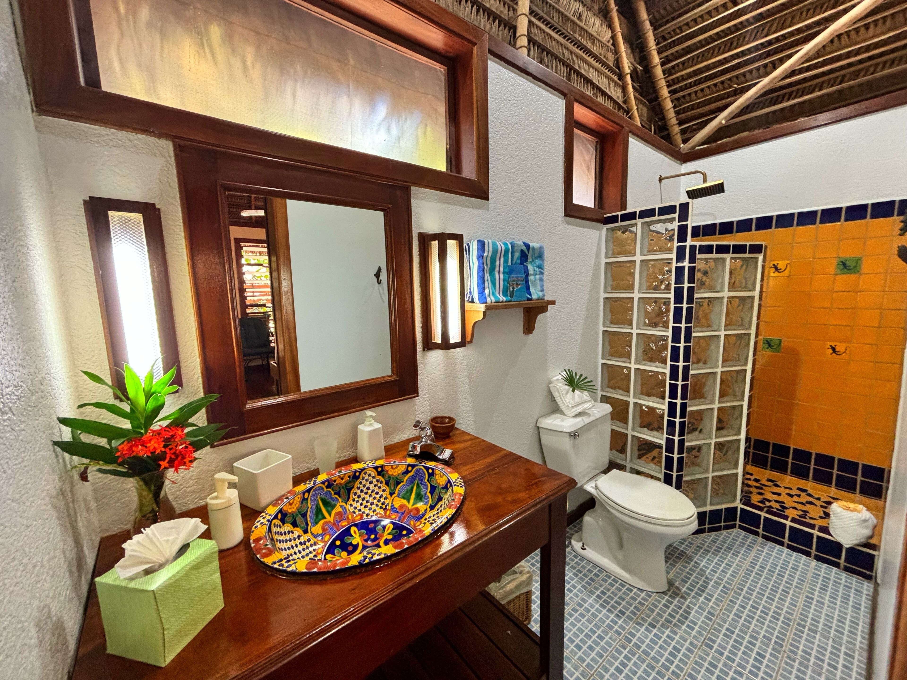 A bathroom with a wooden vanity, a mirror, a toilet, and a shower area with tiled walls.