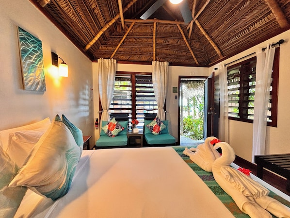 A hotel room with a bed, two seating areas, a window with shutters, and a door leading outside. - Azure Del Mar (Placencia)