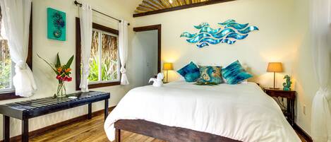 A bedroom with a wooden floor, a bed with white bedding, two bedside lamps, and a wall art piece.