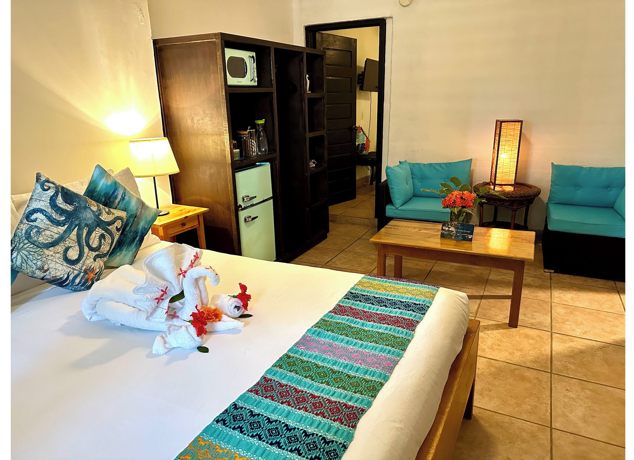 Ein Hotelzimmer mit Bett, Schreibtisch, einer Sitzecke und einer Küchenzeile, sowie einer Tür zu einem weiteren Raum.