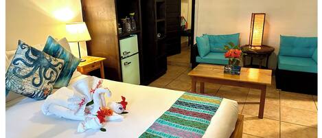 Ein Hotelzimmer mit Bett, Schreibtisch, einer Sitzecke und einer Küchenzeile, sowie einer Tür zu einem weiteren Raum.