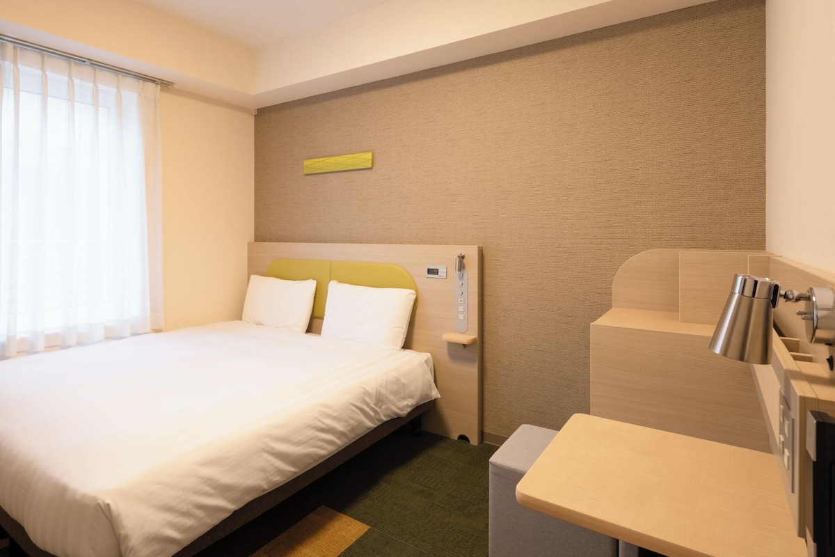 Ein Hotelzimmer mit Bett, Schreibtisch und Bedienfeld an der Wand.