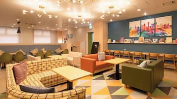 Relax in a comfortable lounge area with sofas, chairs, and a communal table, surrounded by contemporary artwork and a geometric patterned floor.