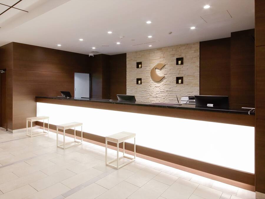 Un mostrador de recepción de diseño moderno, con una encimera de color claro y una pared de piedra con un logotipo abstracto de gran tamaño. Hay dos sillas blancas frente al mostrador.