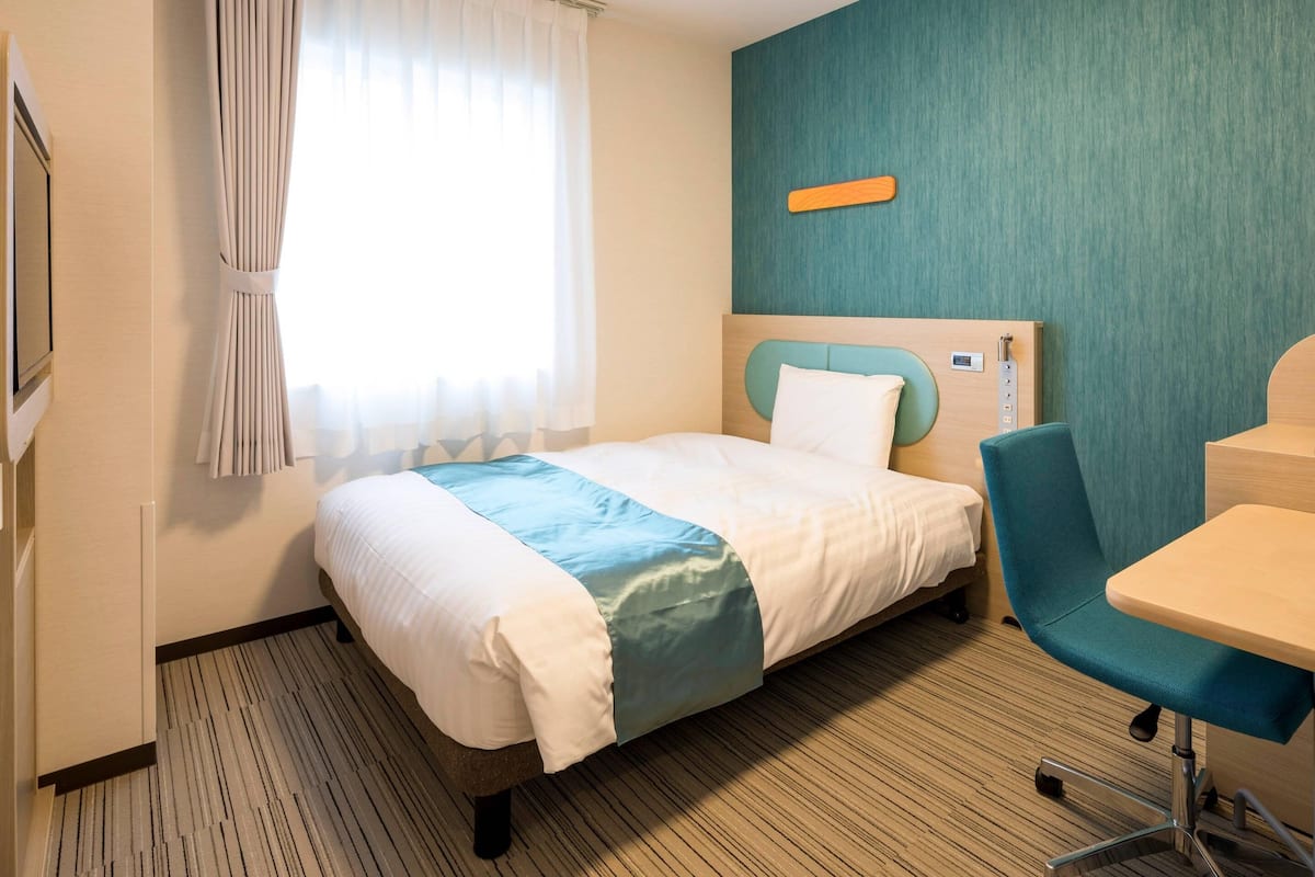 A hotel room with a bed, a desk, and a chair.