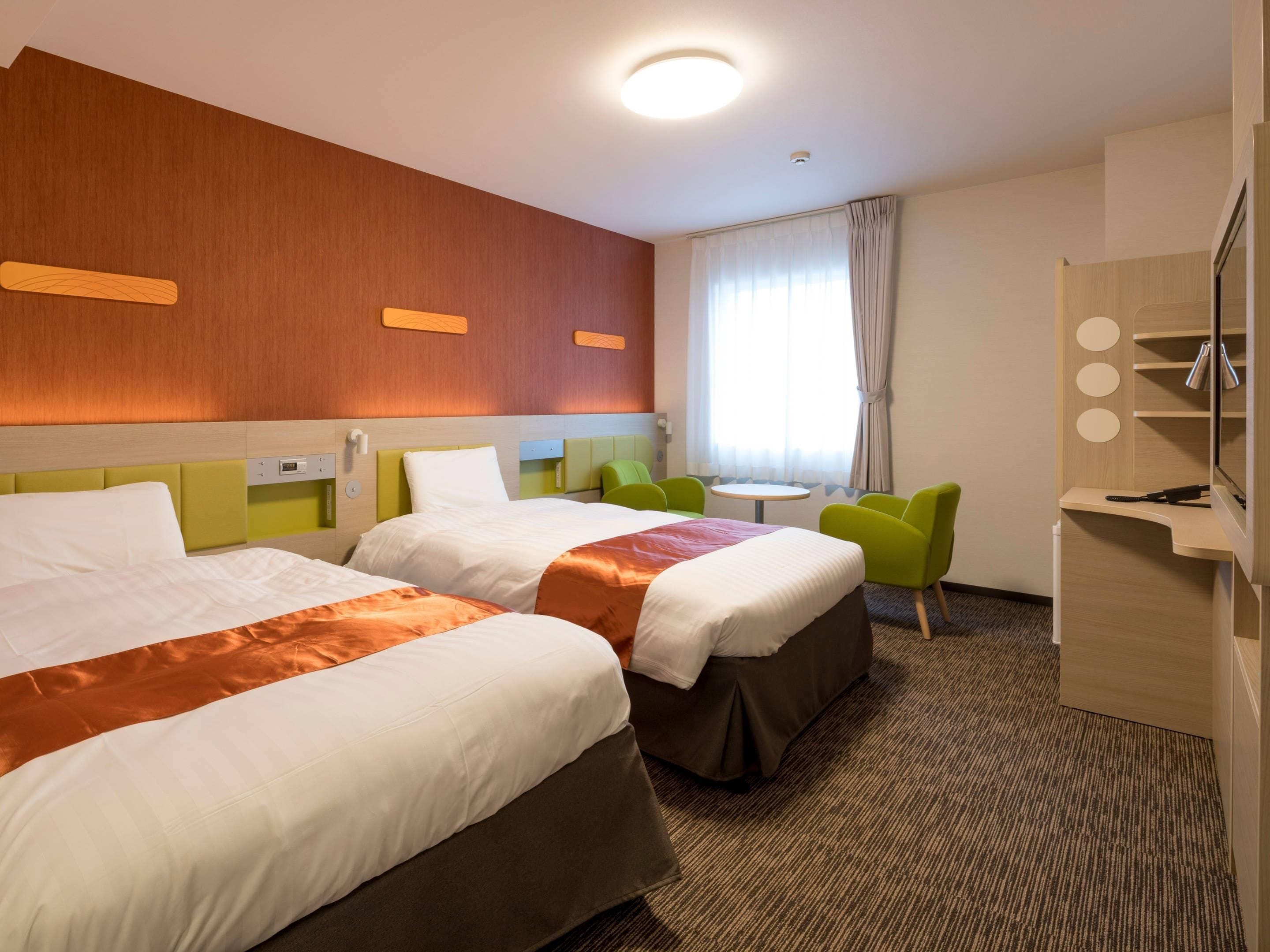 A hotel room with two beds, a desk with a chair, a small table, and a mirror.