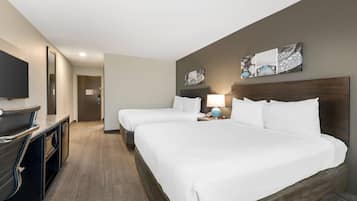 A hotel room with two beds, a desk with a flat-screen TV, a lamp, and artwork on the wall.