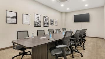 Una sala de conferencias con una larga mesa, varias sillas, un televisor de pantalla plana y cuadros enmarcados en la pared.