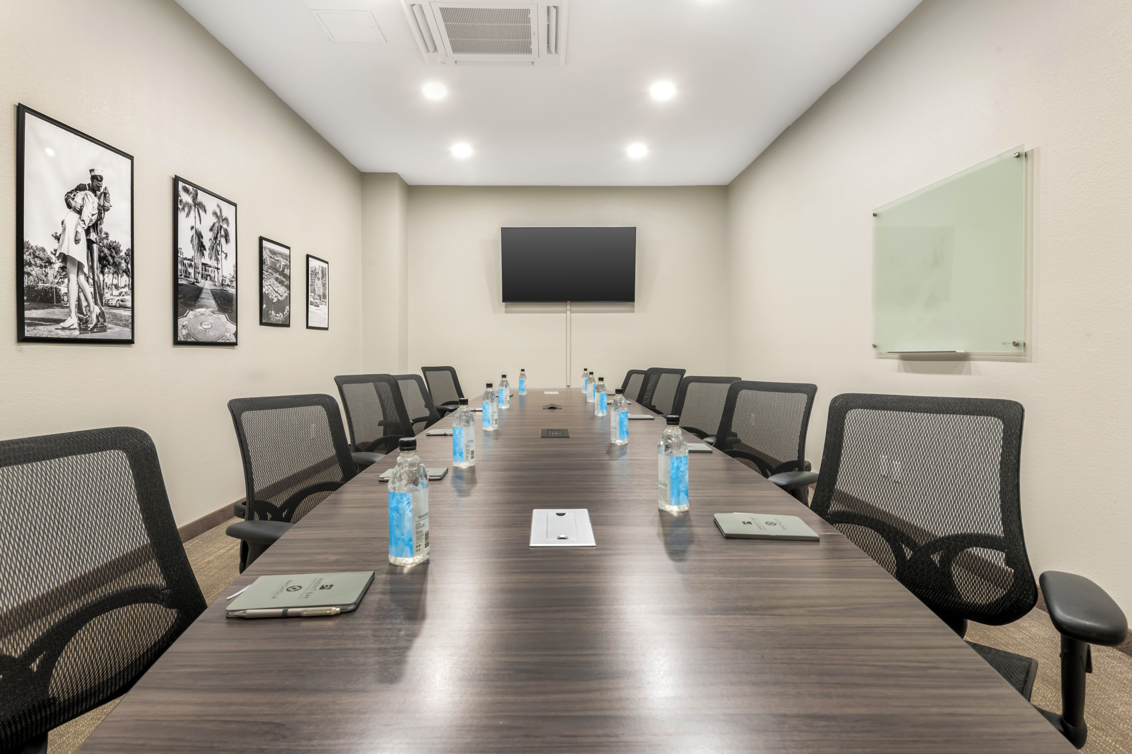 Un salón de conferencias con una larga mesa, sillas, botellas de agua, una pizarra blanca y fotografías enmarcadas en la pared.