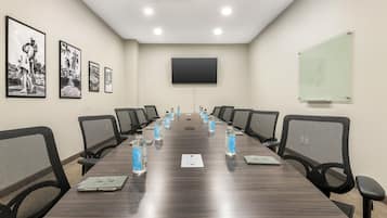 Un salón de conferencias con una larga mesa, sillas, botellas de agua, una pizarra blanca y fotografías enmarcadas en la pared.