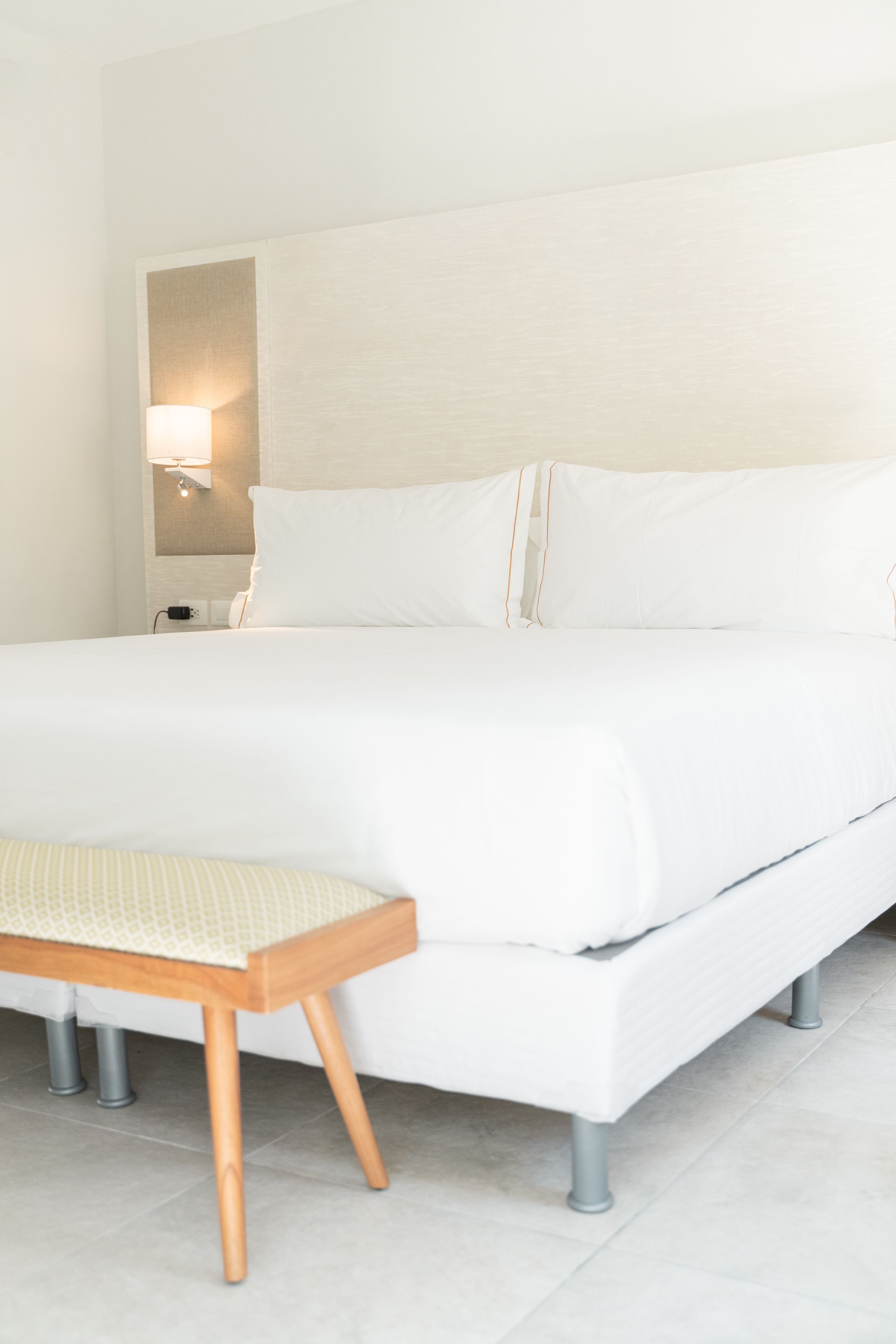 A neatly made bed with white linens and a wooden bench at the foot.