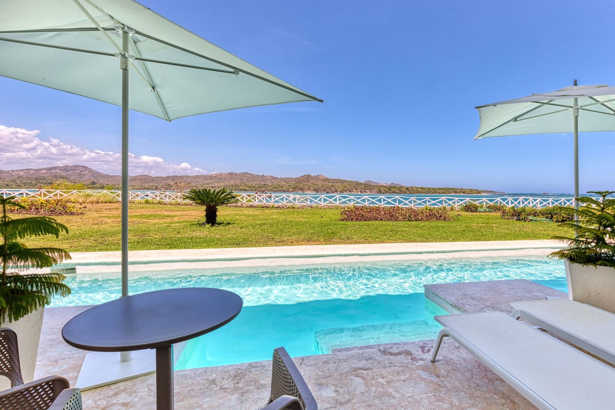 Ein Poolbereich mit zwei Sonnenschirmen, einem Tisch und Liegestühlen.