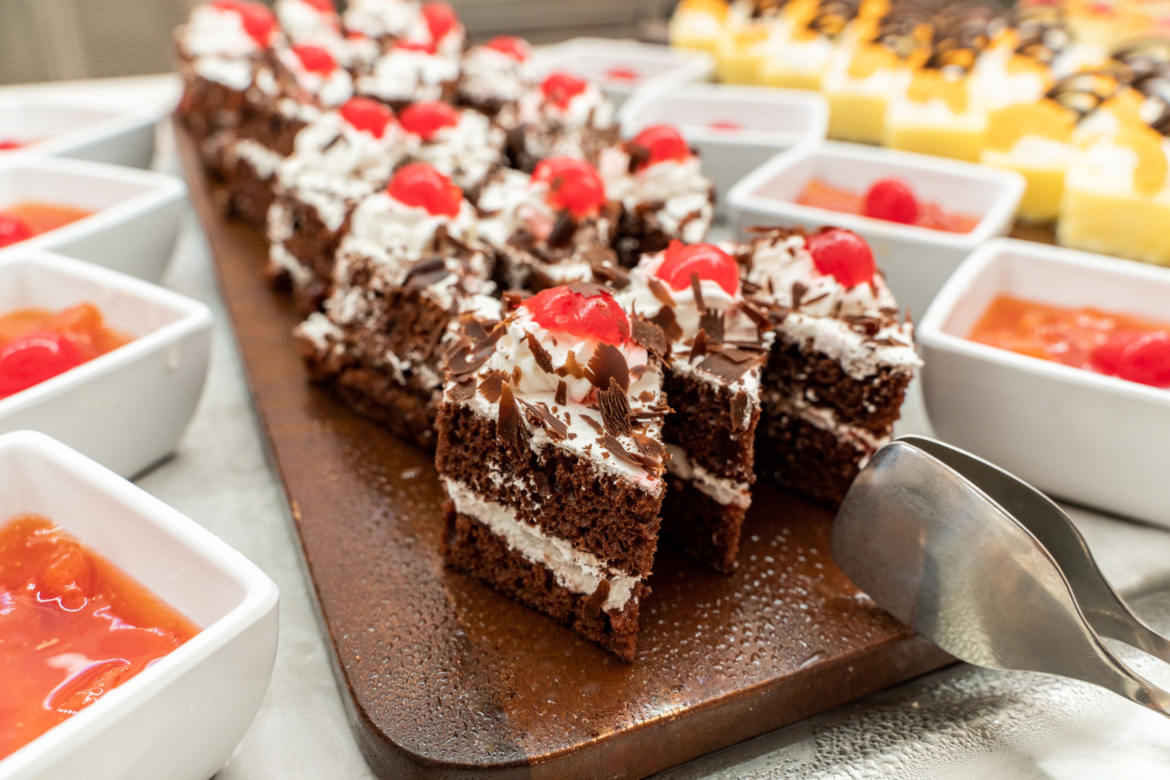 A dessert tray with chocolate cake slices topped with whipped cream and cherries, accompanied by small bowls of sauces.