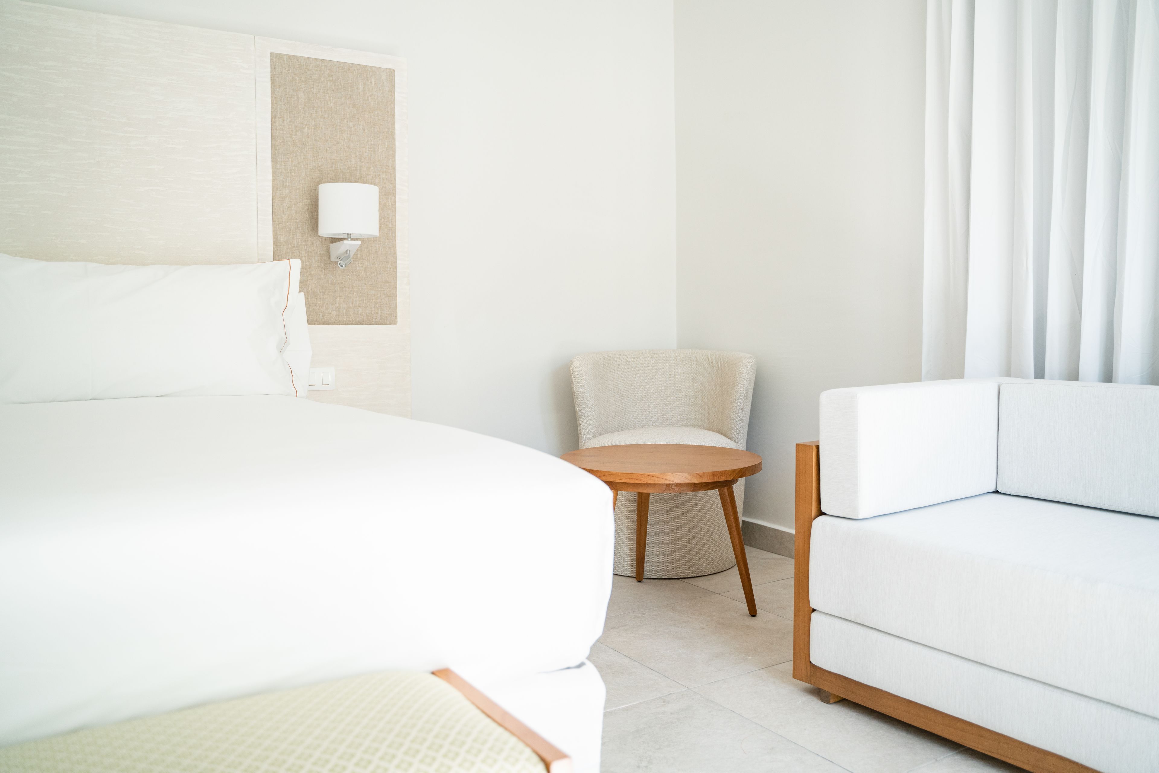 A hotel room with a large bed, a small round table, a sofa, and a wall-mounted lamp.