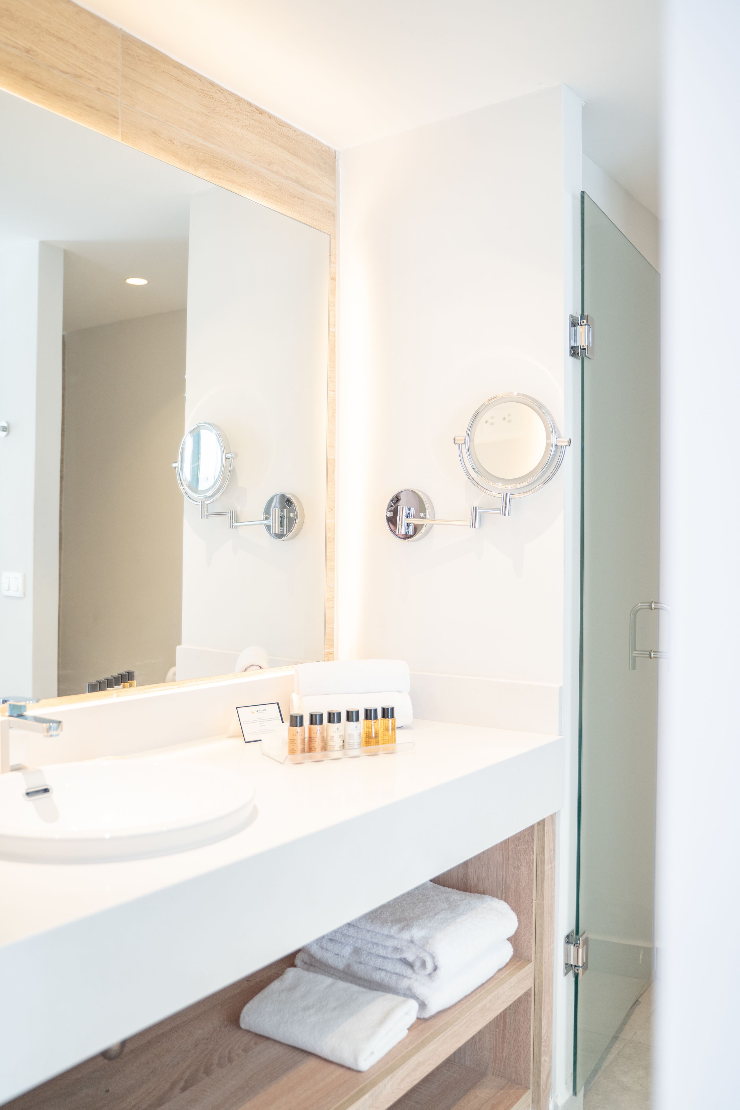 A modern bathroom with a large mirror, a sink, and a glass shower door.