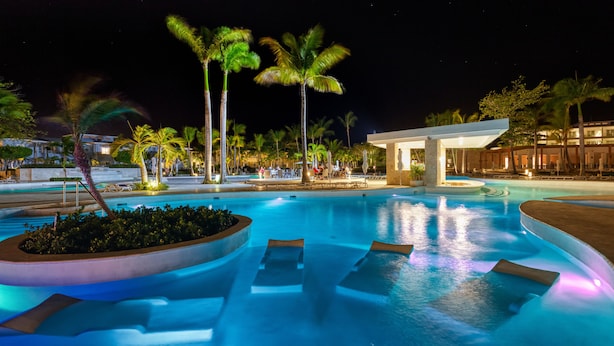 A nighttime resort pool area with lounge chairs and palm trees. - Senator Puerto Plata - All inclusive (Puerto Plata)