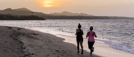 Two people running on a beach with a sunset in the background.