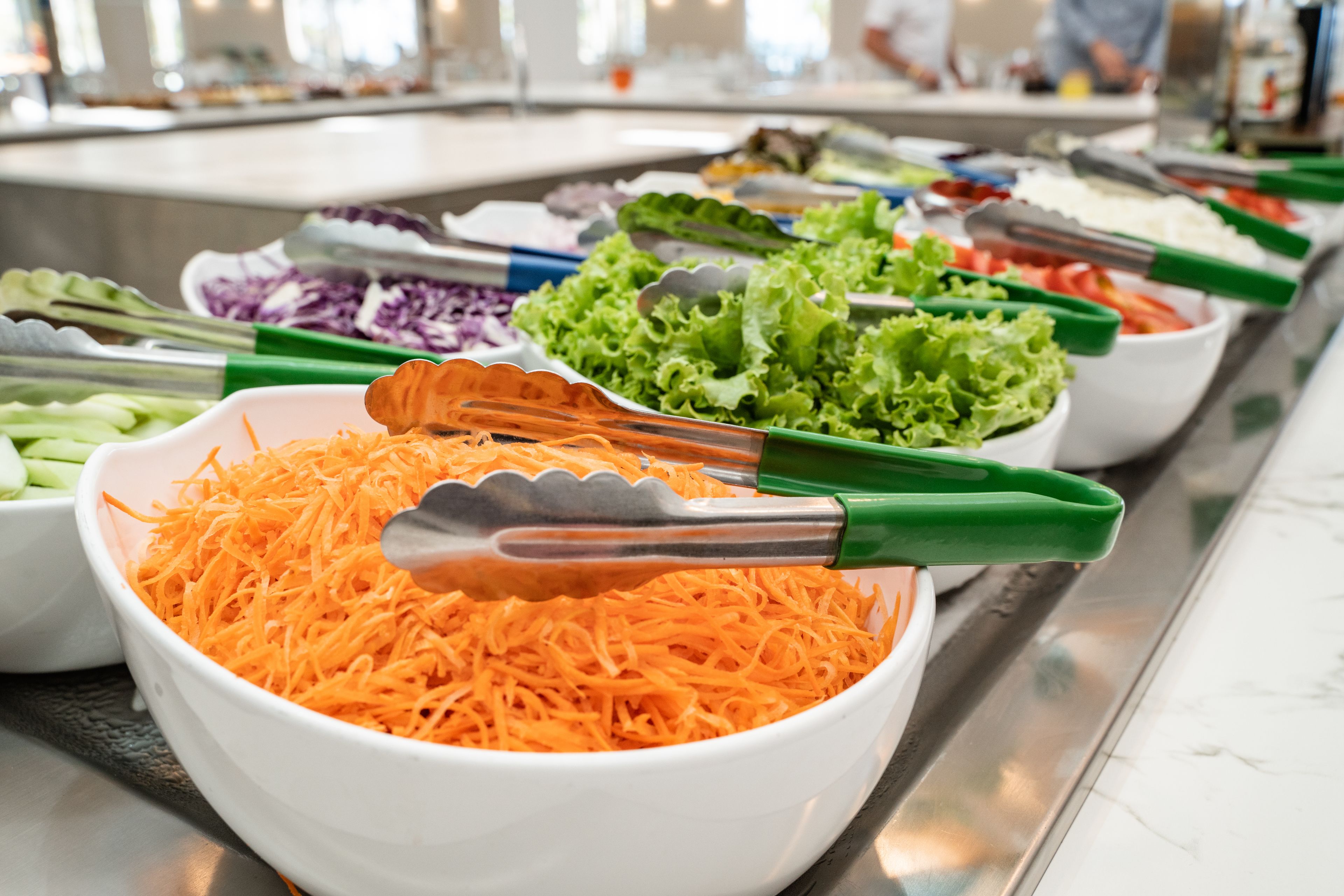 Un buffet proposant une variété de plats, notamment des carottes râpées, de la laitue et d’autres légumes.