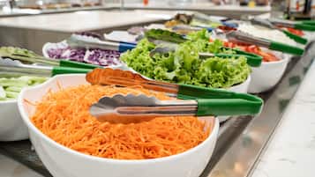 Un buffet proposant une variété de plats, notamment des carottes râpées, de la laitue et d’autres légumes.