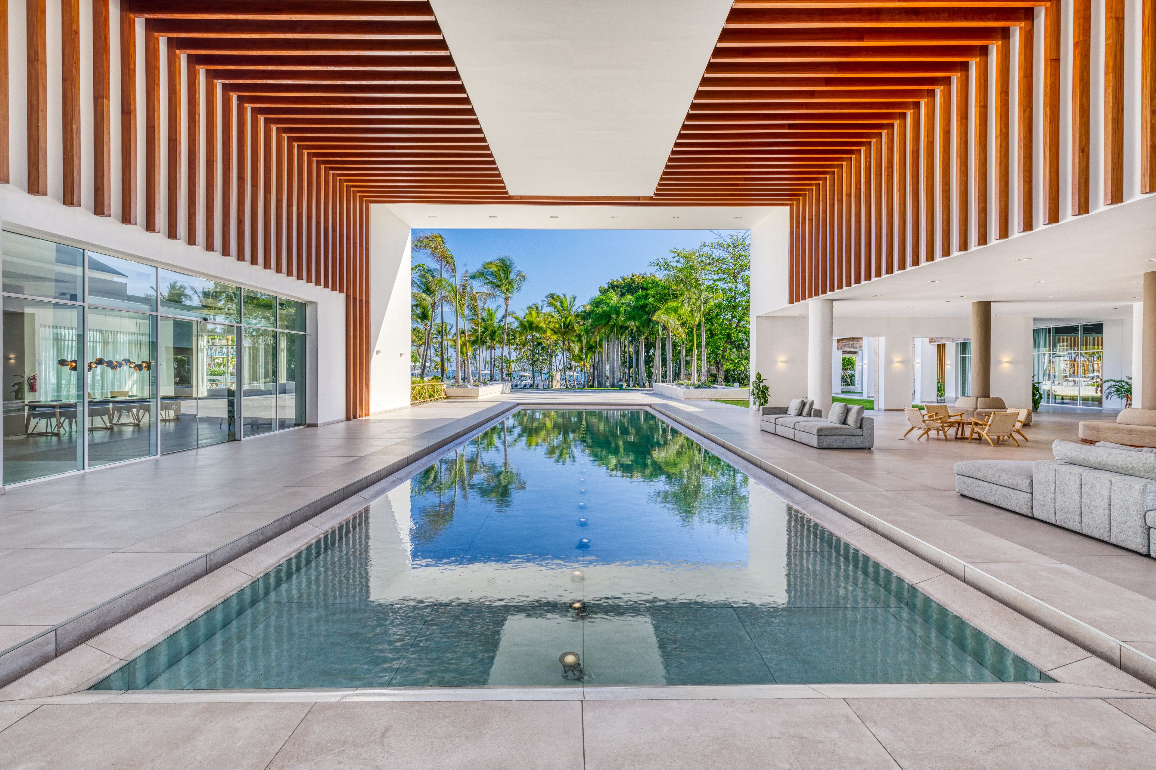 A modern indoor pool area with a clear view of palm trees and a pool reflecting the sky.