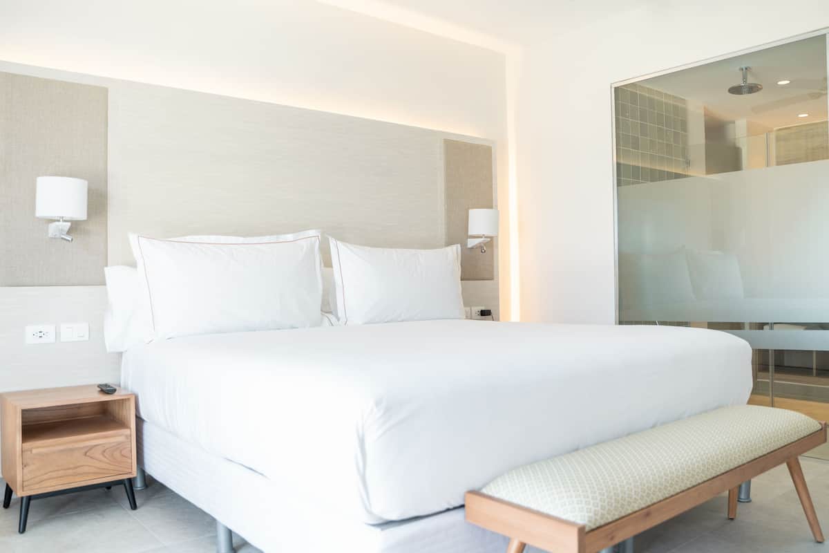 Ein modernes Hotelzimmer mit einem großen Bett, Nachttischen, einer Bank und einer Trennwand aus Glas.