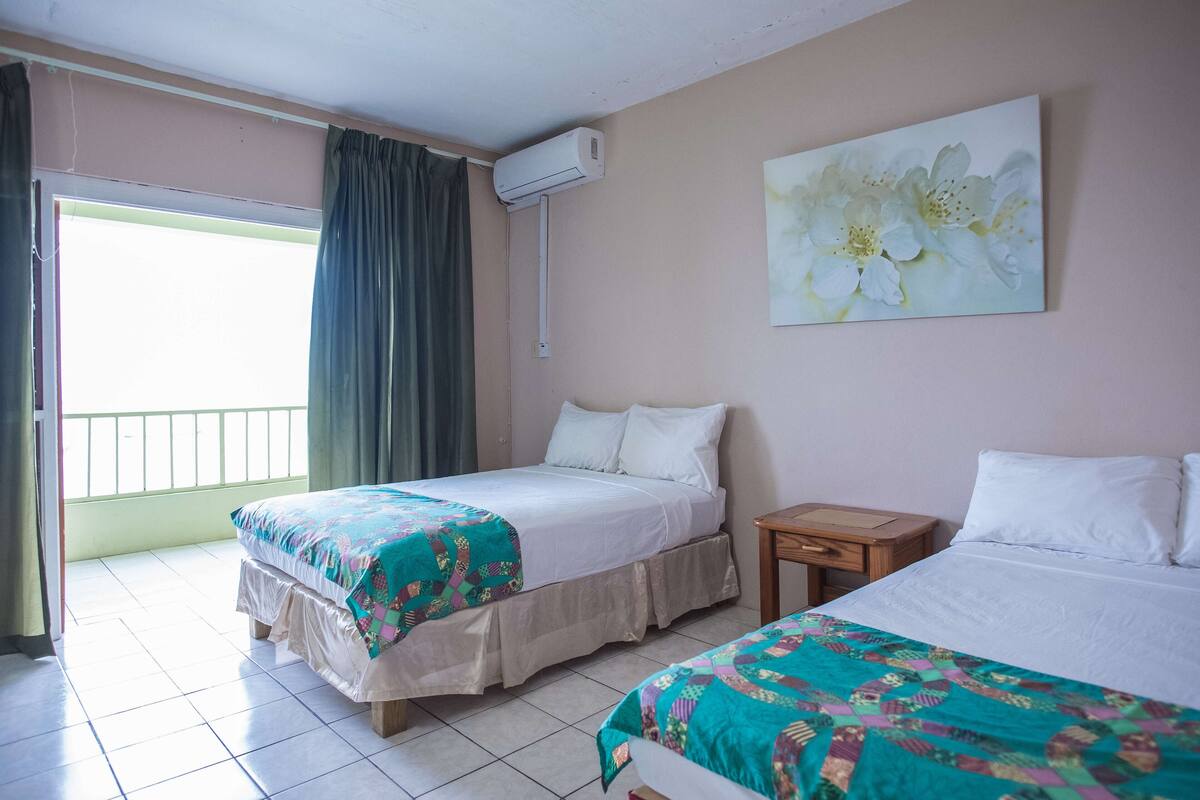 Ein Hotelzimmer mit zwei Betten, einem Fenster mit Vorhängen, einer Klimaanlage und einem Bild an der Wand.