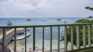 A balcony with a view of the sea, several boats, and a building with a thatched roof. - Ocean Rooms at Oceans Palm Resort (Ocho Rios)
