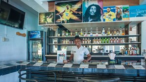 A bar area with a bartender, shelves of liquor bottles, and a television screen. - Ocean Rooms at Oceans Palm Resort (Ocho Rios)